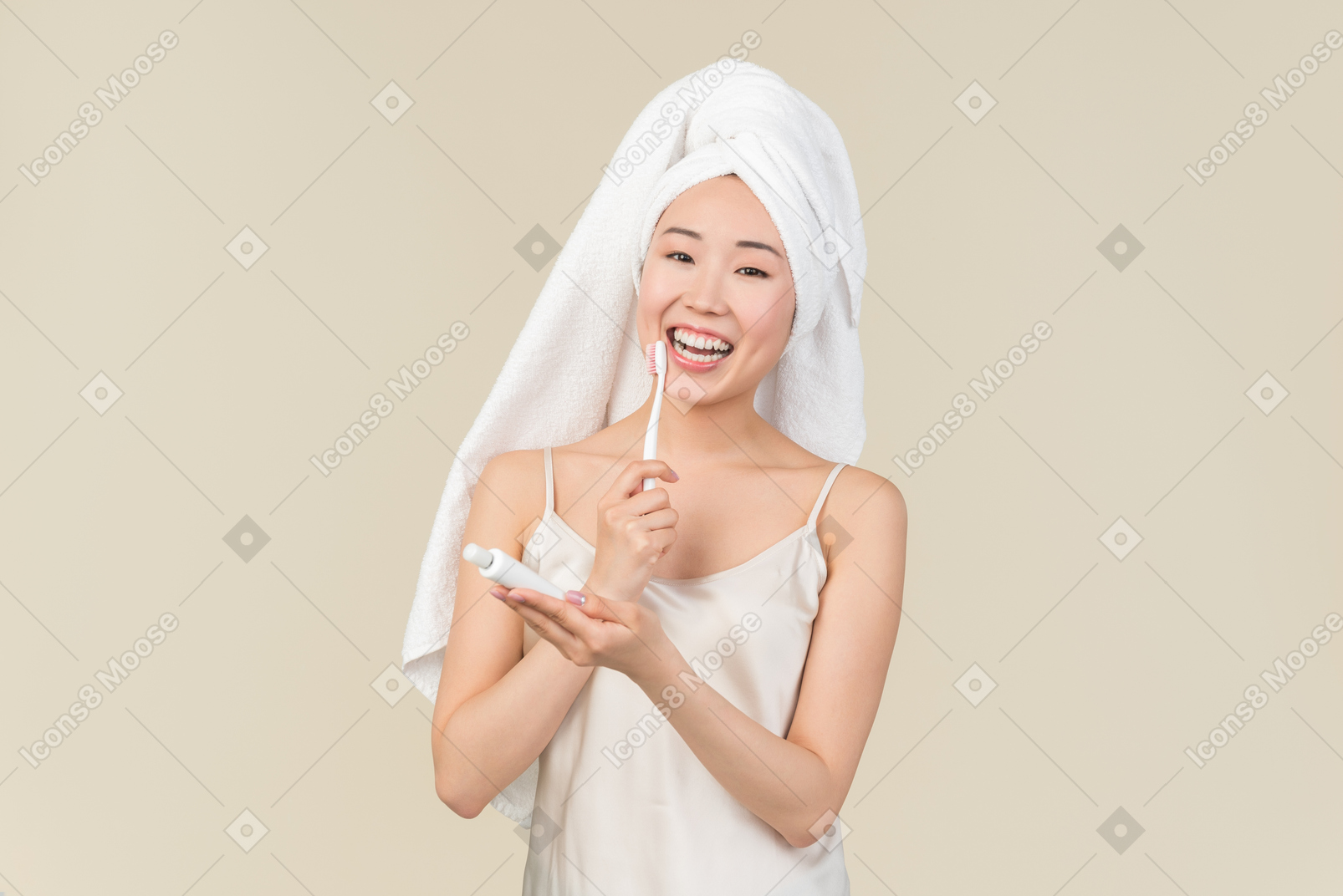 Souriante jeune femme asiatique aux cheveux enveloppé dans une serviette se brosser les dents