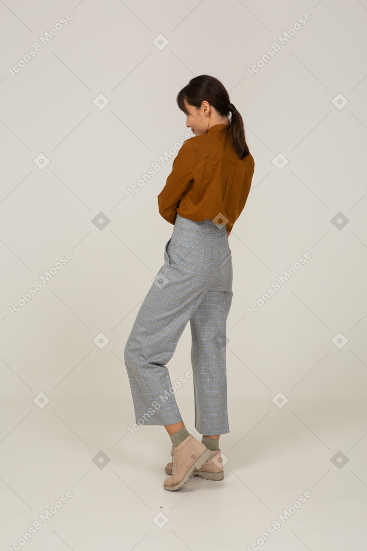 Three-quarter back view of a young asian female in breeches and blouse crossing arms