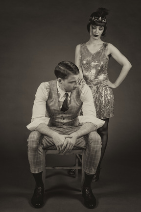 Stylish young lady standing next to a well-dressed gentleman sitting on a chair