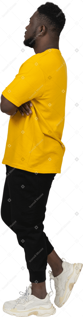 Side view of a suspicious young dark-skinned man in yellow t-shirt crossing arms