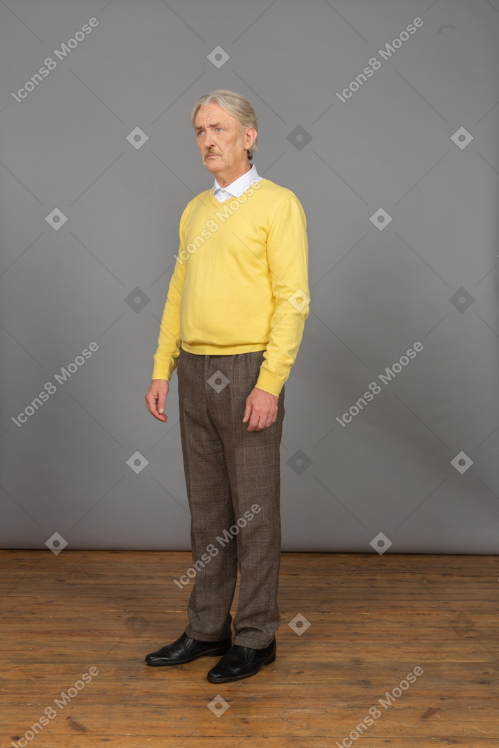 Vista de tres cuartos de un anciano triste en jersey amarillo parado y mirando a un lado