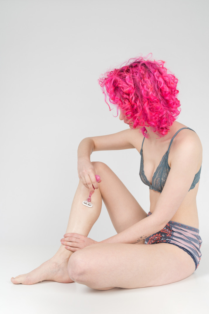 Teenage girl with curly pink hair shaving legs