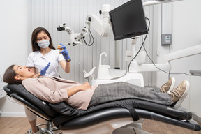 A figura intera di una dentista che mostra il prototipo di denti a una paziente in un gabinetto di ospedale