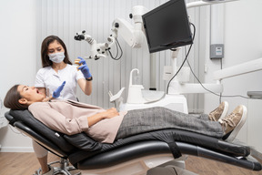 Full-length of a female dentist showing teeth prototype to female patient in a hospital cabinet