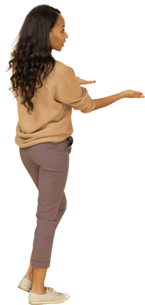 Three-quarter back view of a questioning dark-skinned young female outstretching hands