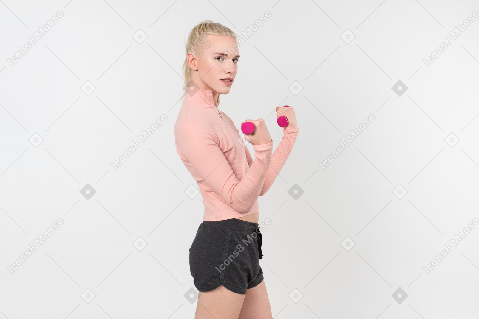 Junge blonde person im schwarzen und rosafarbenen outfit, das mit sporteinzelteilen gegen einen hellgrauen hintergrund aufwirft