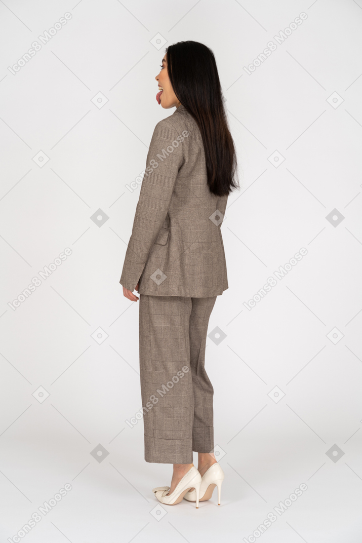 舌を示す茶色のビジネススーツの笑顔の若い女性の4分の3の背面図