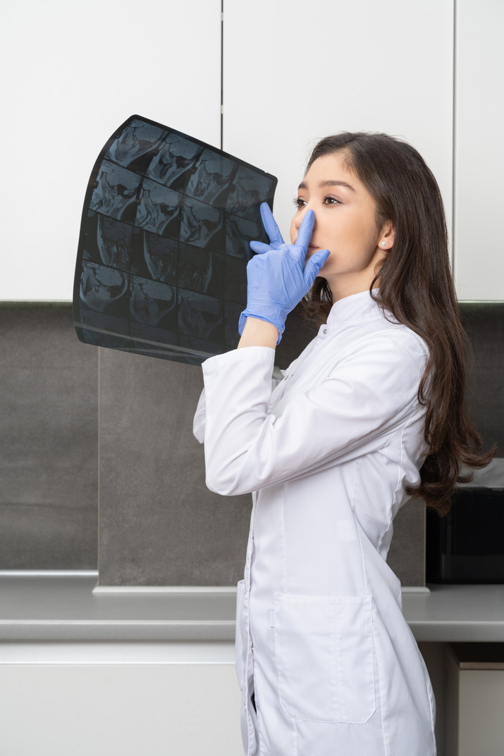 Side view of a female doctor holding an x-ray image and touching nose while looking aside