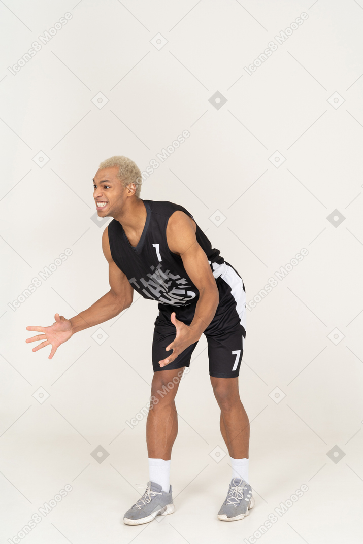 Vista de três quartos de um jovem jogador de basquete do sexo masculino questionador, inclinado para a frente