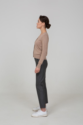 一位年轻女士站在套头衫和裤子放在一边看的侧视图