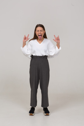 Vista frontal de una joven rockero gritando en ropa de oficina mostrando la lengua