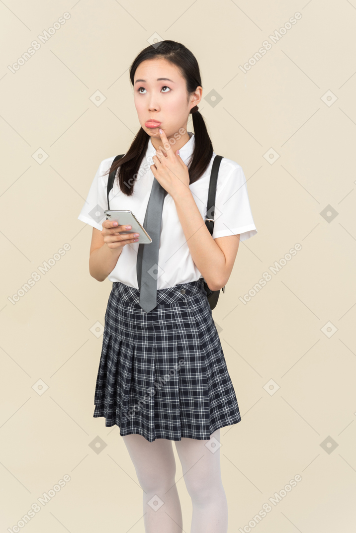 Sad looking asian school girl thinking while using phone