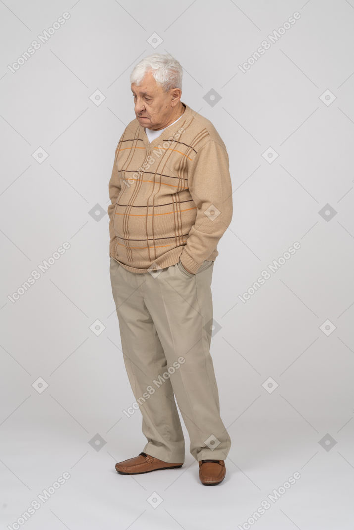 Vorderansicht eines traurigen alten mannes in freizeitkleidung, der mit den händen in den taschen steht
