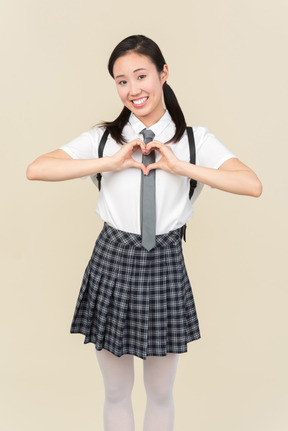 Cheerful asian school girl showing heart gesture with both hands