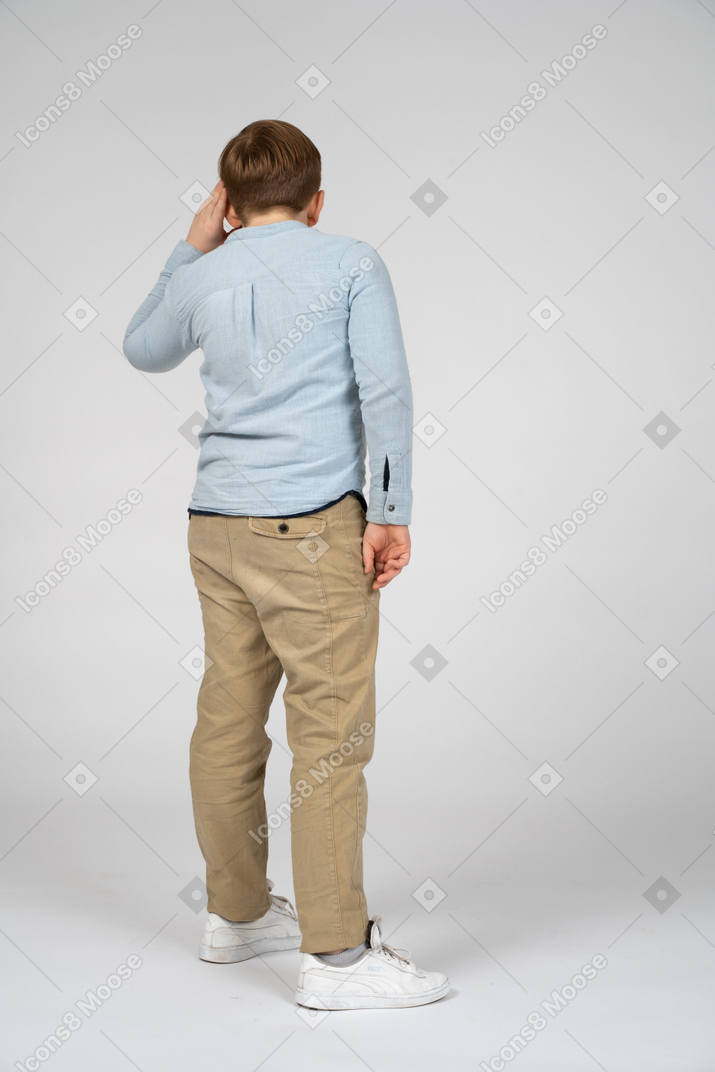 Back view of a boy keeping hand near ear and listening attentively