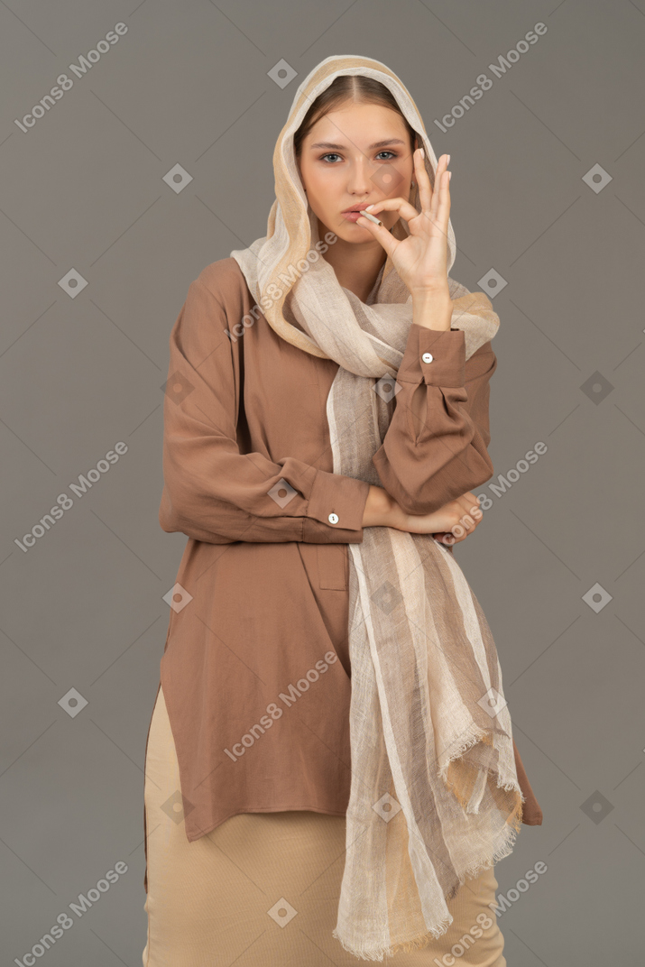Young woman in headscarf and beige clothes smoking a cigarette