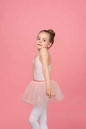 Little ballet dancer standing in profile and holding her tutu