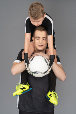 彼の首に小さな男の子を保持しているサッカー選手のクローズアップ