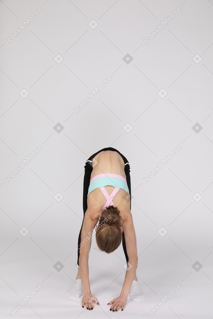 Vue latérale d'une adolescente en tenue de sport accroupie et mettant les mains sur les hanches