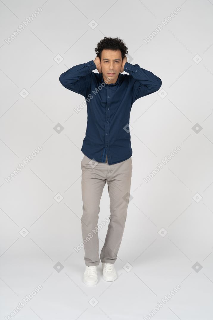 Vista frontal de um homem em roupas casuais cobrindo as orelhas com as mãos