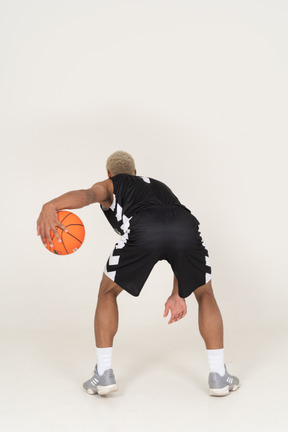 Vista traseira de um jovem jogador de basquete fazendo dribles