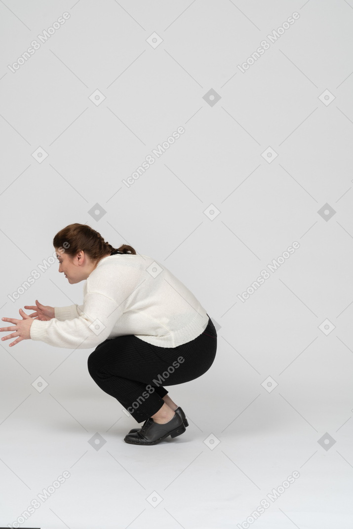 Пухлая женщина в повседневной одежде сидит на корточках, вид сбоку