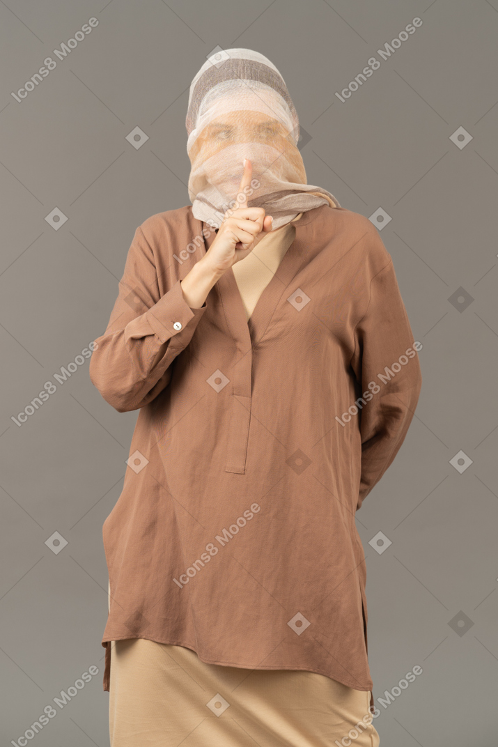 Mulher coberta com xale mostrando um gesto de silêncio