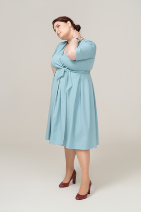 Vista laterale di una donna in abito blu che soffre di dolore al collo