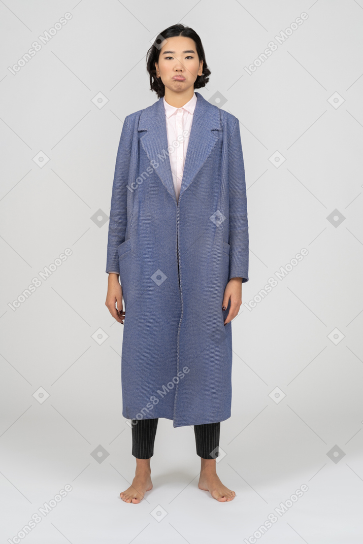 Sad looking young asian woman in long blue coat standing