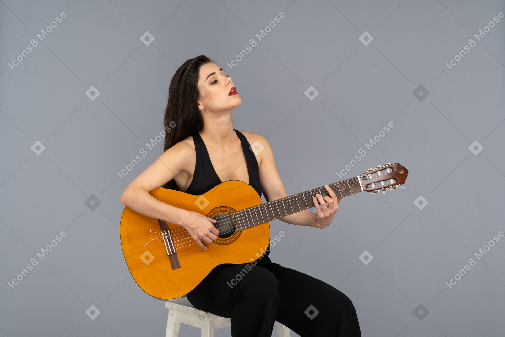 기타를 잡고 머리를 올리는 검은 정장에 앉아있는 젊은 아가씨의 3/4보기