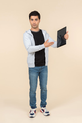 Joven hombre caucásico apuntando a la tableta digital que está sosteniendo