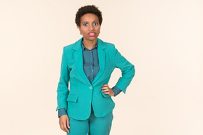 Black woman with a short haircut, wearing all blue, standing against a plain pastel background, looking emotional