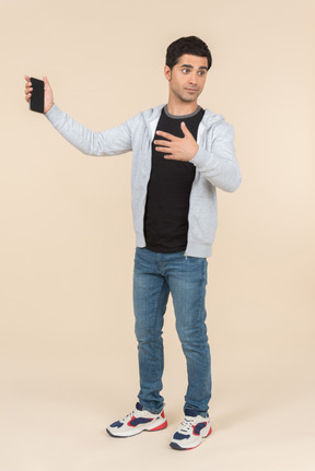 Young caucasian man pointing at smartphone he's holding