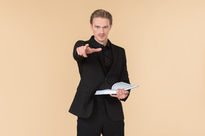 A white man in a fully black suit holding the quran