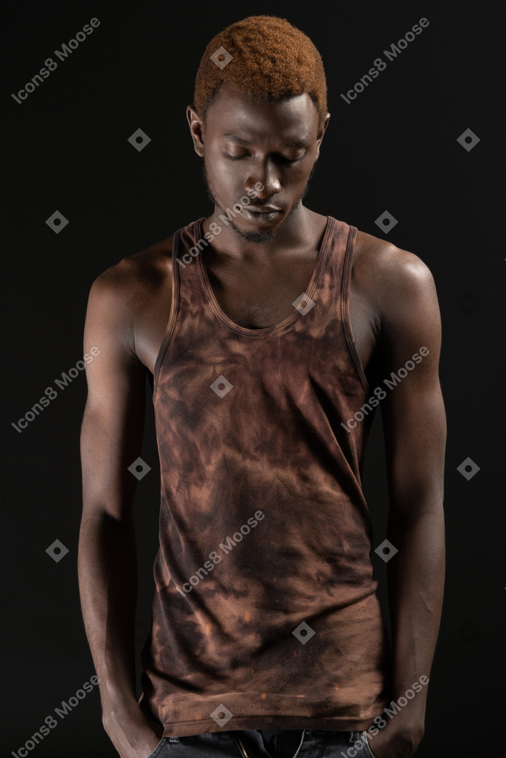 Close-up an african young male standing with his hands in pockets and looking down