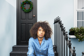 Afro-haired man sitting at christmas decorated porch