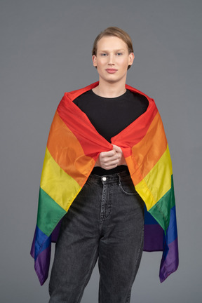 Nonbinary person standing wrapped in lgbtq+ flag