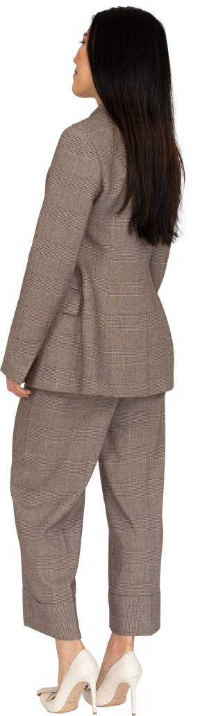 Three-quarter back view of a pleased smiling young lady in brown business suit