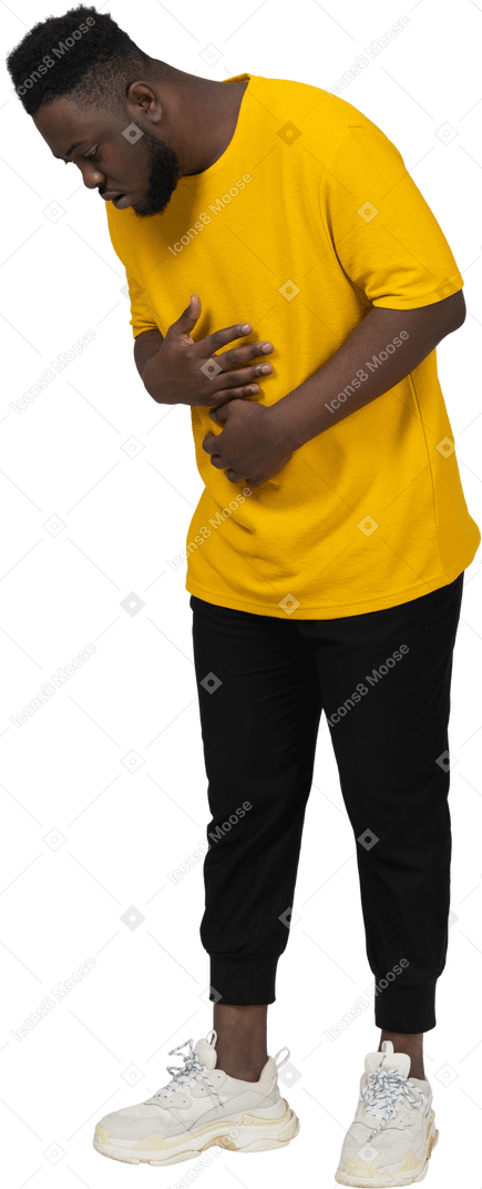 Three-quarter view of a young dark-skinned man in yellow t-shirt touching stomach & looking down