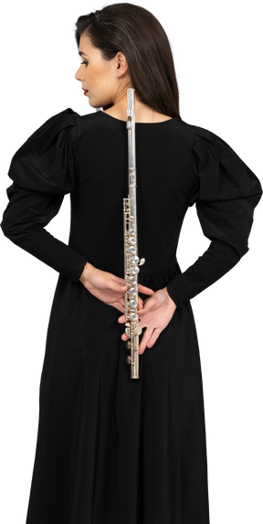 Vista traseira de uma jovem de vestido preto segurando uma flauta atrás