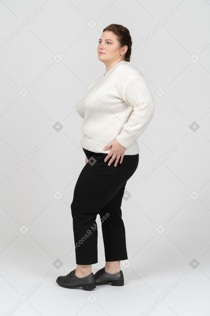 頭の後ろで手で立っている白いセーターのふっくらした女性