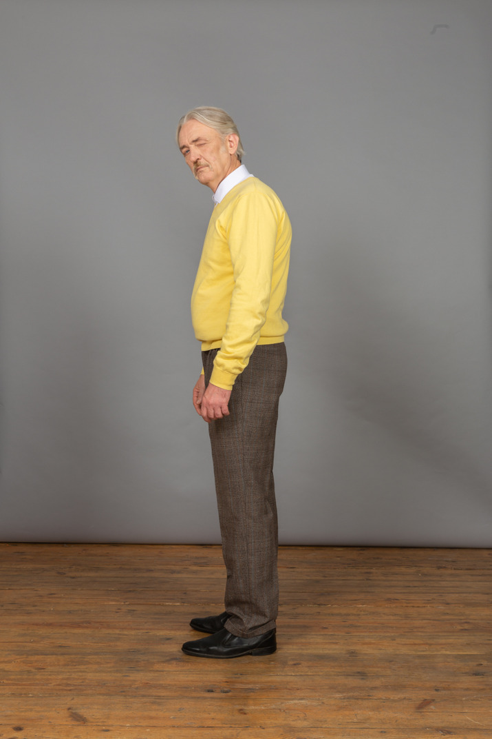 Side view of an old curious man in yellow pullover turning head and winking