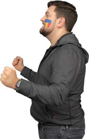 Side view of a satisfied male football fan with colorful face art clenching fists