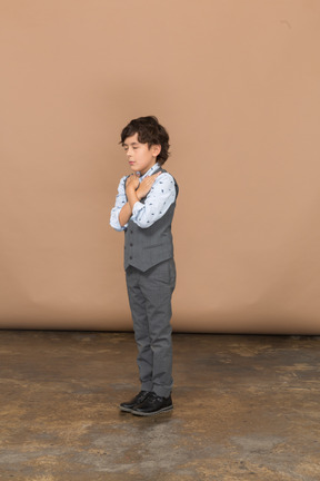 Vista frontale di un ragazzo carino in abito grigio in piedi con le mani sulle spalle