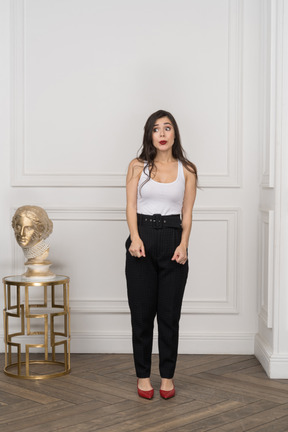 Front view of a shy young female looking aside while standing near golden greek sculpture