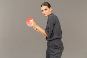 Side view of young woman in a jumpsuit serving tennis ball