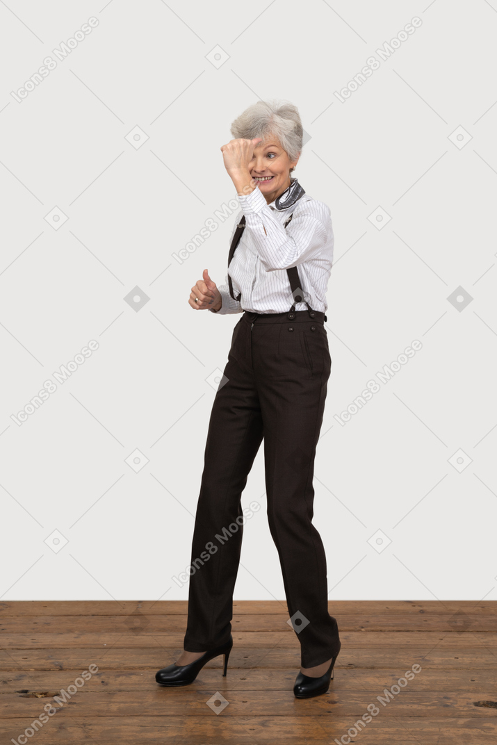 Three-quarter view of a smiling old lady in office clothing raising her hand