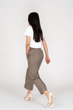 Vista posteriore di tre quarti di una giovane donna che cammina in calzoni e maglietta