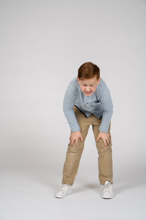 Vista frontal de um menino curvando-se e tocando os joelhos doloridos