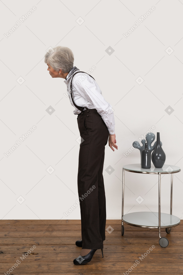 Vista laterale di una vecchia signora curiosa in abiti da ufficio sporgendosi in avanti